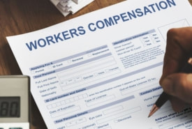Hand holding a pen and filling out a workers’ compensation form.